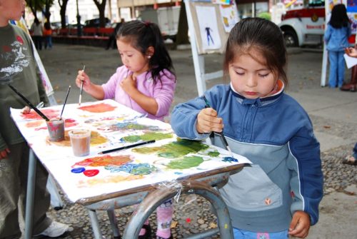  Two kids in long sleeves painting on a white canvas during sessions